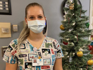 Nicole, in a mask, standing next to a Christmas tree