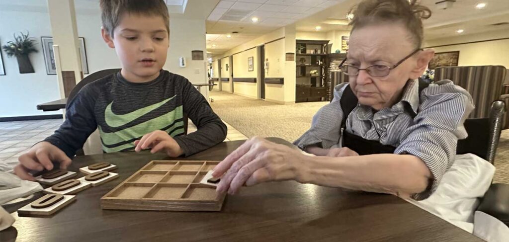 Young volunteer Archer plays Tic-Tac-Toe with resident Bev during intergenerational activities at Baptist Health & Rehab, a senior living community.