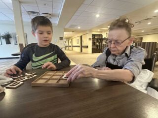 Young volunteer Archer plays Tic-Tac-Toe with resident Bev during intergenerational activities at Baptist Health & Rehab, a senior living community.